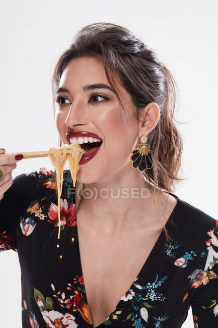Модная женщина со стильным макияжем смотрит прочь с лапшой во рту и с помощью палочек для еды изолированы на белом фоне — стоковое фото