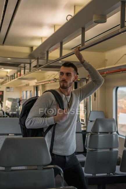 Giovane concentrato con lo zaino tenendo corrimano mentre in piedi in vagone della metropolitana vuoto — Foto stock