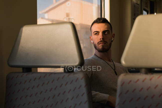 Pensativo joven pasajero masculino escuchando música en el vagón del metro - foto de stock