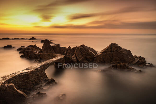 D'en haut de roche rugueuse au milieu de la mer tranquille avec brouillard et ciel nuageux coloré en soirée — Photo de stock
