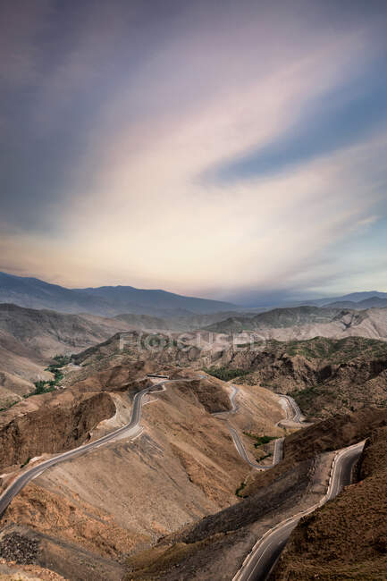 D'en haut de la route serpentine étroite dans les montagnes brunes puissantes sous ciel bleu nuageux coloré — Photo de stock