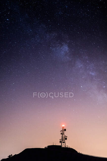 Von unten der Funkturm mit rotem Licht oben unter hellem Nachthimmel mit leuchtenden Sternen — Stockfoto