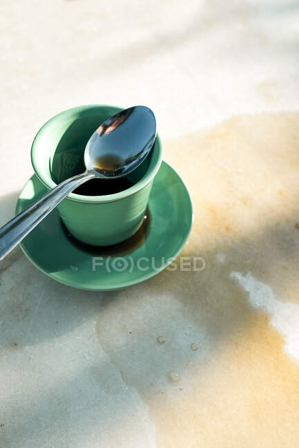 Do acima mencionado copo de cerâmica verde de café preto quente derramado na mesa composta com colher de chá de metal no pires na mesa cinza — Fotografia de Stock