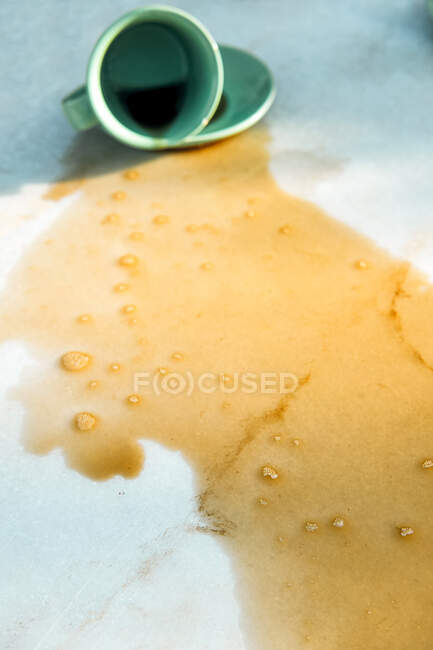 Hot aromatic brown beverage spilling from dropped cup on saucer to table — Stock Photo