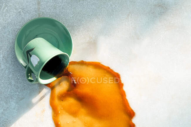From above warm brown drink flowing from dropped green ceramic mug on saucer to gray table on cafe terrace — Stock Photo