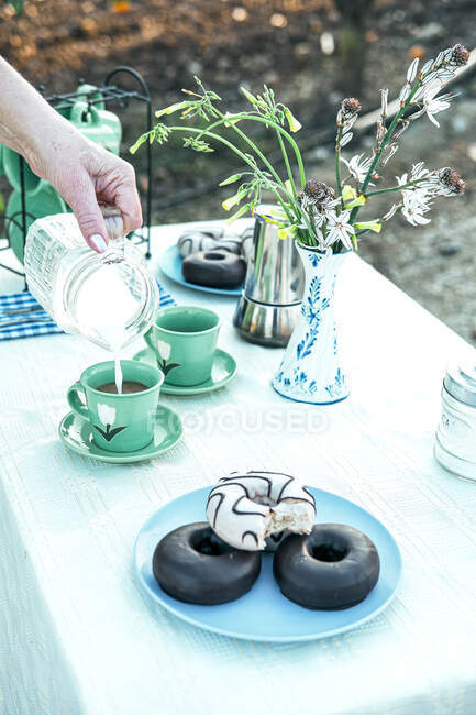 Woman pouring fresh milk from jug to ceramic mug while having picnic in garden — Stock Photo