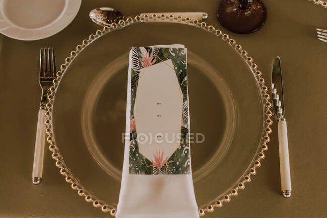 From above of white napkin and colorful postcard on stylish green plate on table with knife spoon and fork in modern restaurant — Stock Photo
