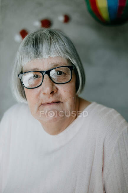 Elderly woman in white blouse standing on light background looking at camera — Stock Photo