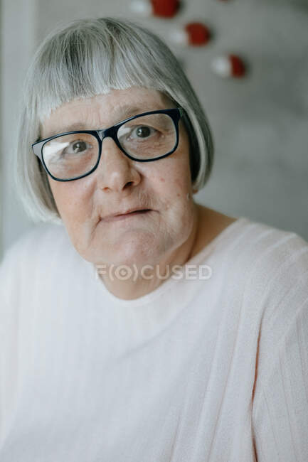 Elderly woman in white blouse standing on light background looking at camera — Stock Photo