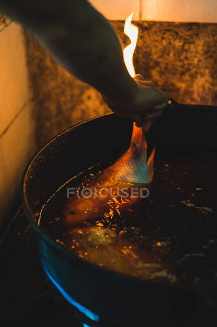 Зверху безликий кухар смажить свіжу рибу у великій сковороді з олією на сільській кухні — стокове фото