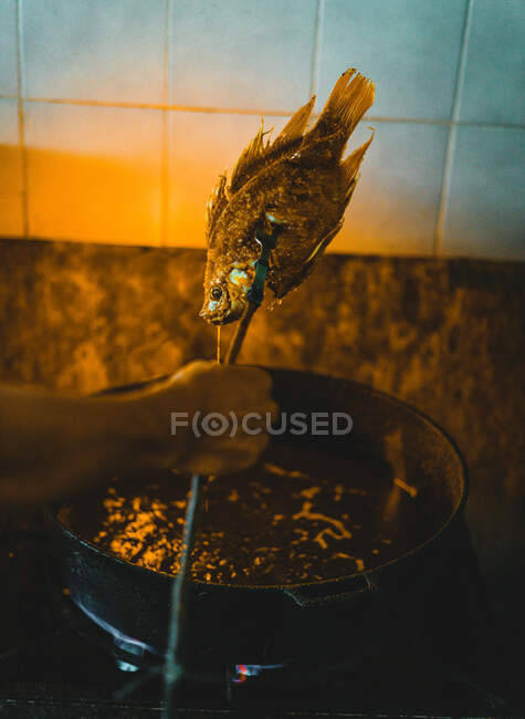 From above crop unrecognizable chef taking out fried fish from oil in rustic kitchen — Stock Photo