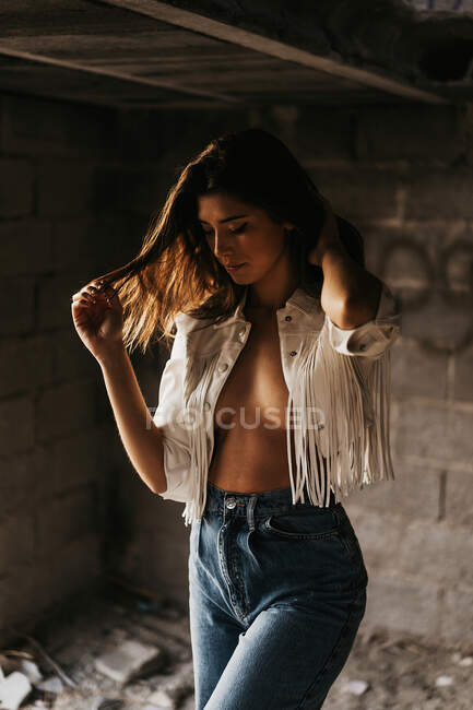 Seductive young gorgeous woman in stylish clothes touching hair while standing inside ruined stone building — Stock Photo