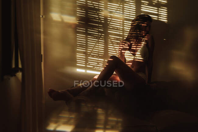 Gesichtslose sinnliche junge Frau in weißer Unterwäsche sitzt auf dem Boden im Sonnenlicht von Schatten im Raum — Stockfoto