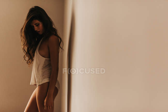Vista laterale di sottile sensuale donna affascinante in mutandine e canotta in piedi a parete in camera — Foto stock