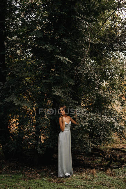 Стильная женщина, опирающаяся на ствол дерева в лесу — стоковое фото