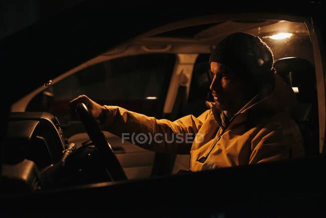 Through glass of serious male in warm clothes at steering wheel while driving car at night — Stock Photo