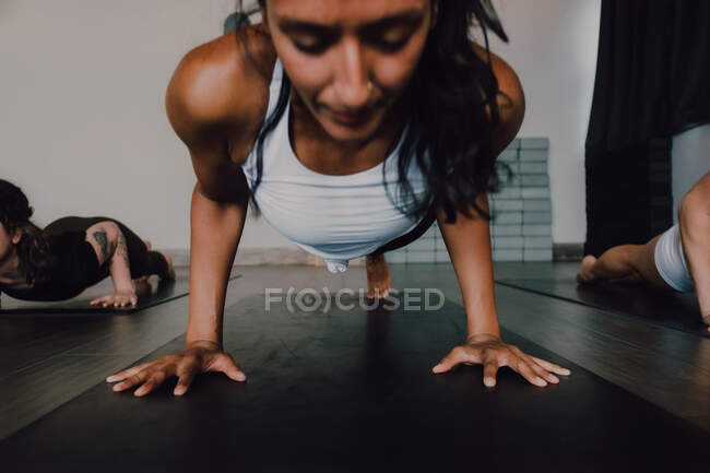 Crop fit barefooted female in sportswear focusing and doing one legged plank pose on sports mat while training with other athletes on floor in spacious modern gym — Stock Photo
