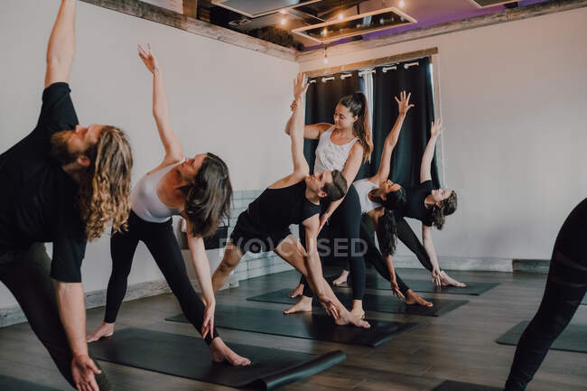 Smiling diligent female instructor in sportswear teaching revolved triangle pose to a group of sporty people doing exercise standing on sports mats in modern workout room — Stock Photo