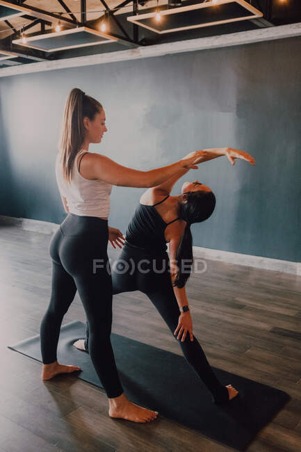 Smiling diligent female instructor in sportswear teaching revolved triangle pose to a group of sporty people doing exercise standing on sports mats in modern workout room — Stock Photo