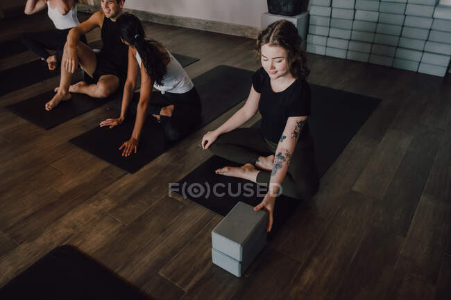 High angle of young diverse women and men in sportswear sitting in lotus pose and having interest discussions while resting after group training in contemporary yoga studio — Stock Photo