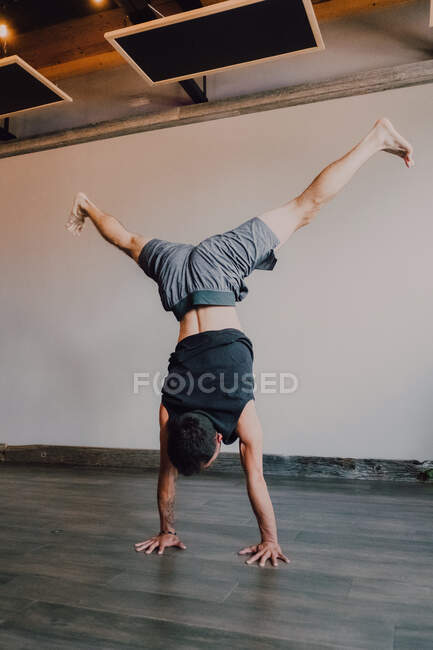 Back view of faceless barefooted man in sportswear standing upside down in downward facing dog pose while training in contemporary gym — Stock Photo