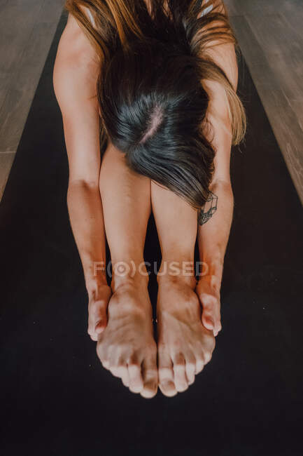Unrecognizable barefooted female in activewear stretching body while doing paschimottanasana pose sitting on sports mat on floor in modern gym — Stock Photo