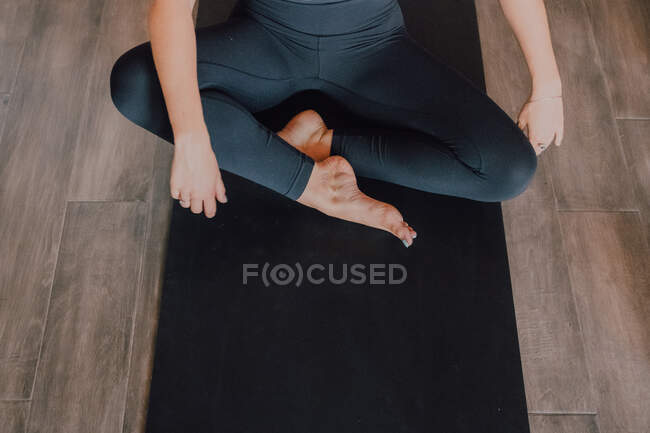 Diligent cropped unrecognizable barefooted woman in sportswear performing bound angle pose exercise on mat in light contemporary gym — Stock Photo