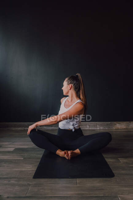 Диліжантна босонога жінка в спортивному одязі, що виконує прив'язаний кут позу вправи на килимок у сучасному спортзалі — стокове фото
