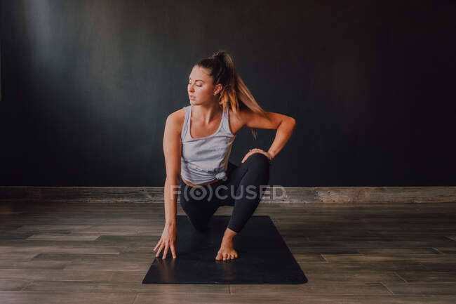 High angle of confident barefooted woman in sportswear stretching body in eka pada rajakapotasana two position on mat and looking away while training in spacious contemporary workout room — Stock Photo