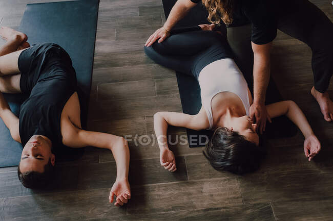 Angle élevé de groupe de jeunes femmes et hommes sportifs en vêtements de sport avec les yeux fermés et les jambes croisées respiration relaxante et profonde tout en étant couché en position savasana et en méditant sur les tapis de sport dans le studio de yoga moderne — Photo de stock