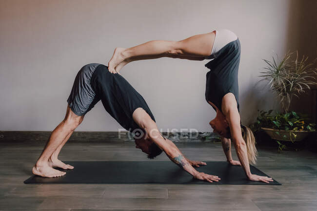 Side view of young barefooted man and focused woman in sportswear doing balance exercise standing in dog pose while training together on floor in light contemporary workout room — Stock Photo