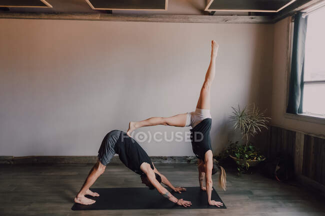 Side view of young barefooted man and focused woman in sportswear doing balance exercise standing in dog pose while training together on floor in light contemporary workout room — Stock Photo