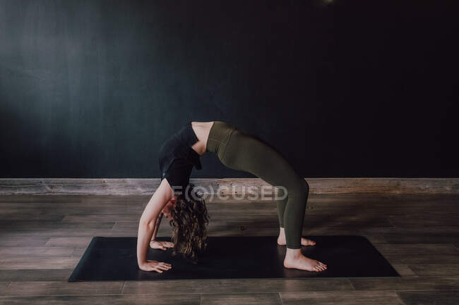 Side view of barefooted woman in sportswear doing urdhva dhanurasana pose in contemporary workout room — Stock Photo