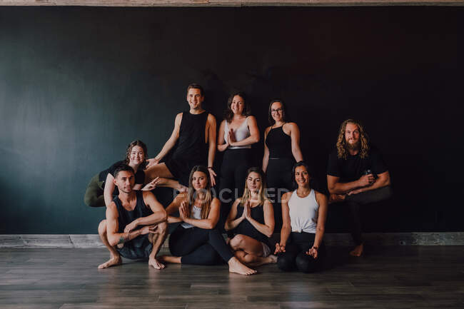 Впевнені тонкі спортивні люди в спортивному одязі, що виконують різні позиції йоги на тлі чорної стіни темної сучасної студії — стокове фото