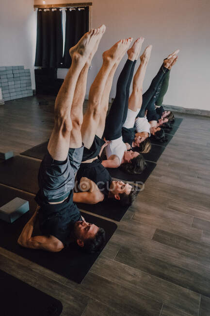 Зліва група дорослих спортсменів у спортивному лаві з розтягнутими ногами в саламбі сарвангасані пози на спортивних матах під час практики йоги в сучасній студії. — стокове фото