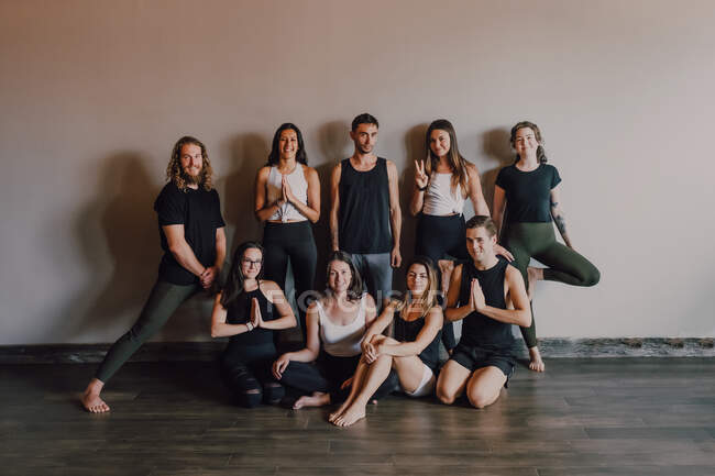 Gente deportiva delgada y segura en ropa deportiva que realiza diferentes posiciones de yoga contra la pared negra del estudio moderno oscuro - foto de stock