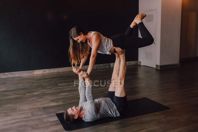 High angle side view of happy young barefooted couple in activewear looking at each other and smiling while doing balance exercise standing in front plank position on floor in contemporary studio — Stock Photo