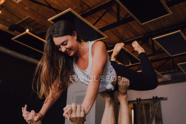 Vue latérale à angle élevé d'un jeune couple heureux pieds nus en vêtements de sport se regardant et souriant tout en faisant un exercice d'équilibre debout en position de planche avant sur le sol dans un studio contemporain — Photo de stock
