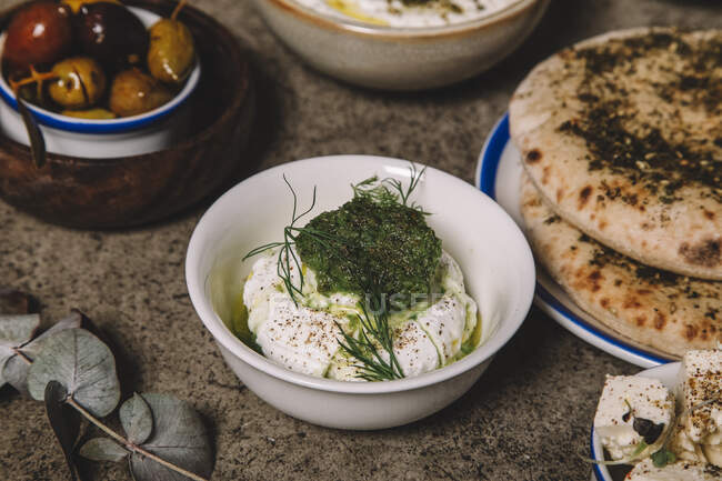 Schüssel Käse mit grüner Soße für Fladenbrot und Oliven auf grauem Tisch — Stockfoto