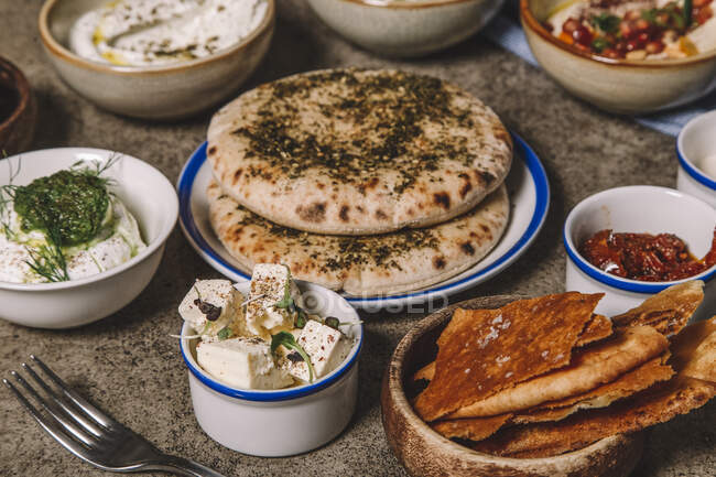 Servierte Gerichte aus Käse, Hummus und Ruckfleisch mit Fladenbrot auf grauem Tisch — Stockfoto