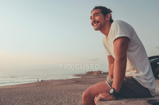 Счастливый человек с мотоциклом наслаждается закатом на пляже — стоковое фото