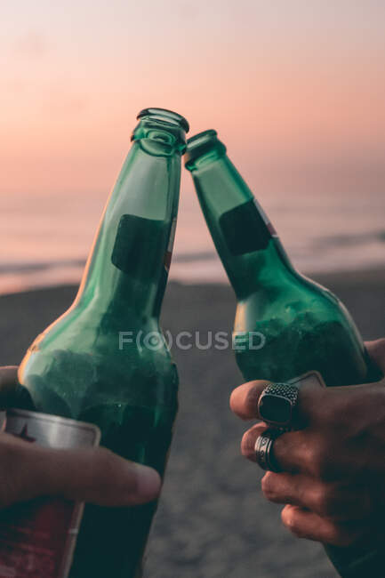 Imagen recortada de amigos tostadas con cerveza en la playa puesta del sol - foto de stock