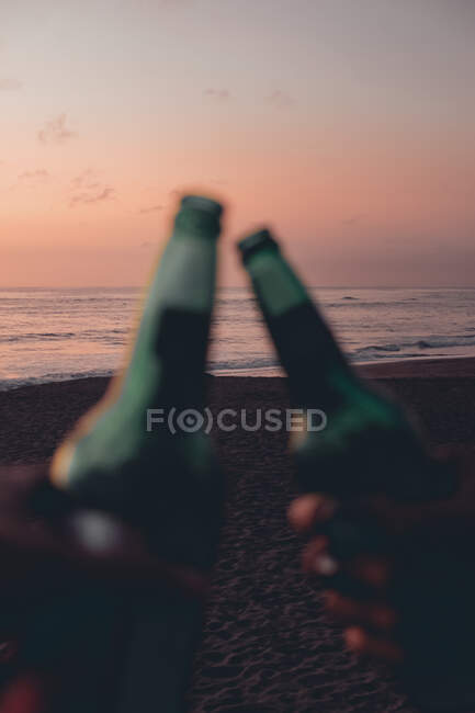 Abgeschnittenes Bild von Freunden, die am Strand von Sonnenuntergang mit Bier anstoßen — Stockfoto