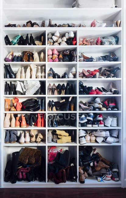 Modern white closet and square shelves with female colorful expensive high heels shoes and sneakers — Stock Photo