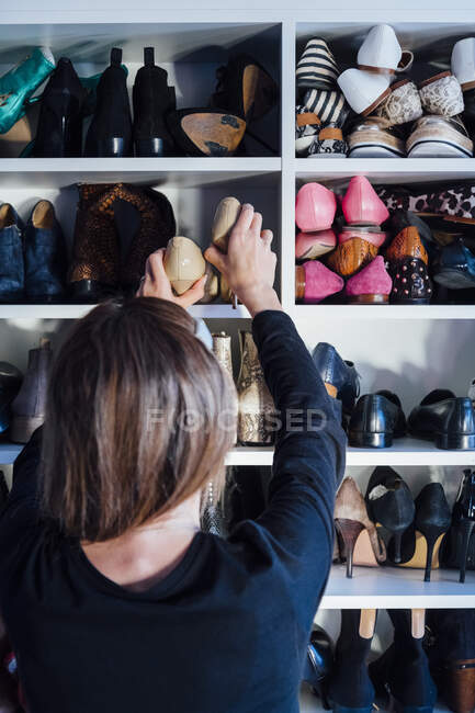 Vista posteriore della donna senza volto che prende scarpe con tacchi alti beige dallo scaffale del moderno armadio bianco — Foto stock