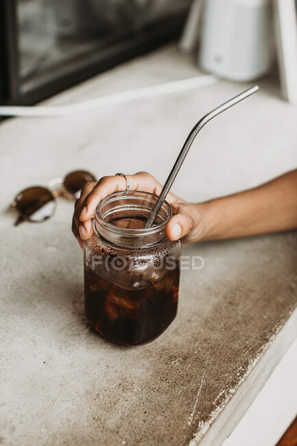 Immagine ritagliata di donna che tiene il bicchiere di cocktail su un piano di lavoro concreto — Foto stock