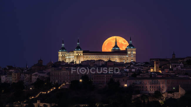 Splendido scenario di palazzo antico illuminato costruito sopra la città nella notte colorata con luna piena rossa a Toledo — Foto stock
