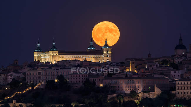 Splendido scenario di palazzo antico illuminato costruito sopra la città nella notte colorata con luna piena rossa a Toledo — Foto stock