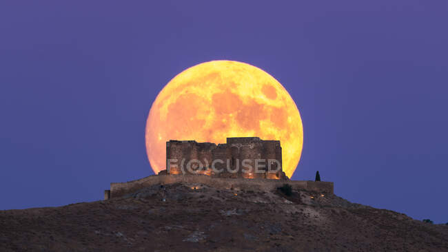 Desde abajo pintoresco paisaje de antigua fortaleza abandonada en la cima de la montaña iluminada por la luna llena por la noche en Toledo - foto de stock