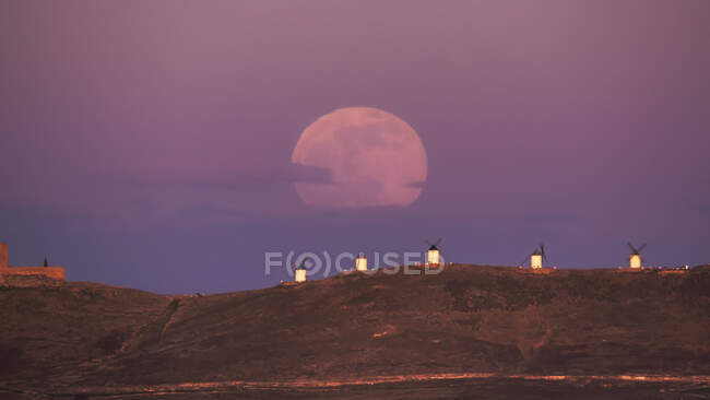 Cenário incrível de majestosa lua cheia sobre o vale com moinhos de vento no pôr do sol — Fotografia de Stock